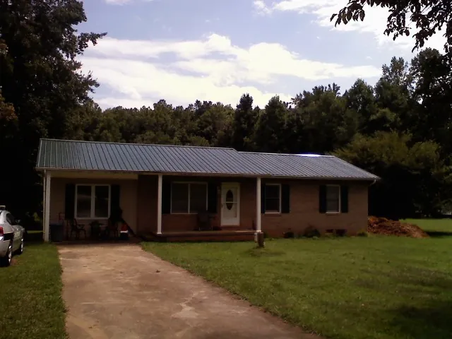 Dark green metal roof on a brick ranch with a covered porch in Ravenna
